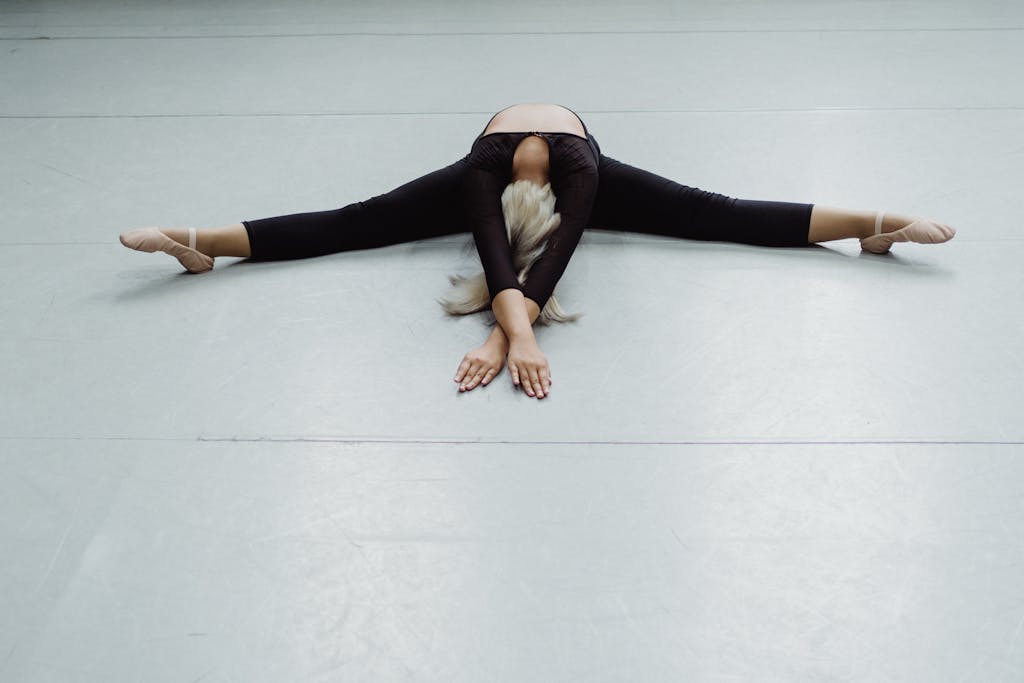 From above full body of anonymous ballerina practicing twine position on floor in choreography hall