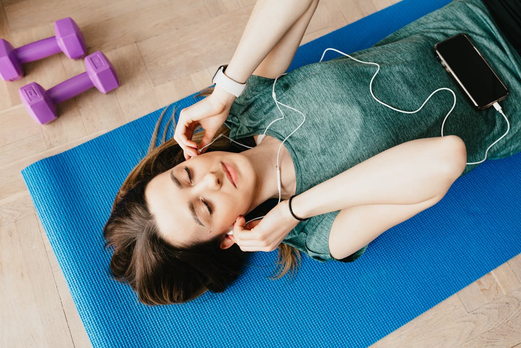 Sportive lady in earphones listening to music chilling on mat