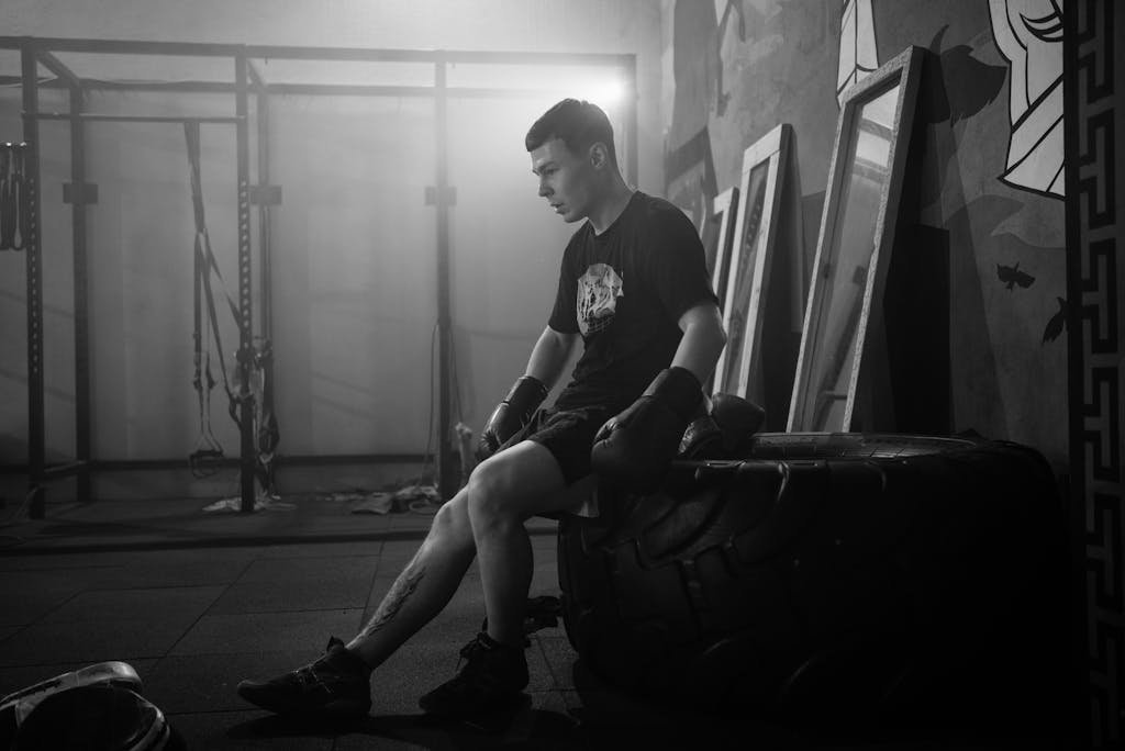 Black and white photo of a boxer resting indoors, showcasing mood and fitness.