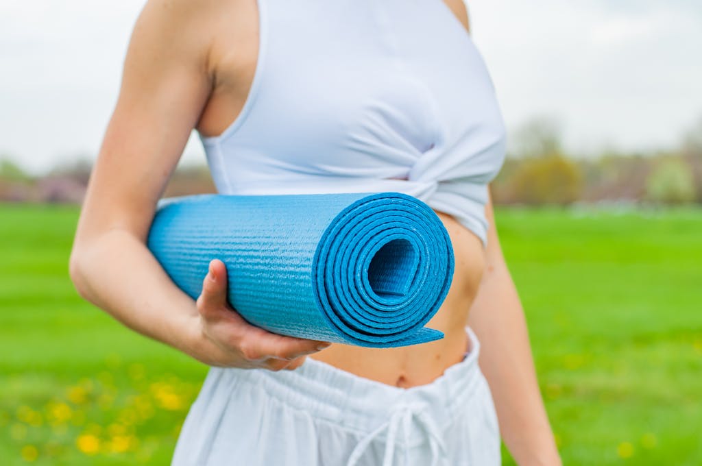 Close-up of a woman holding a blue yoga mat in a green outdoor setting during spring.